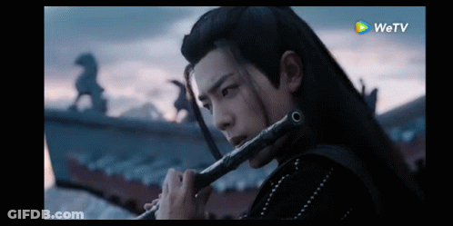 Man With Long Hair Playing Flute In Dark Room GIF