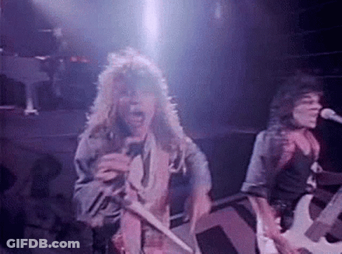 Man With Long Hair Singing Into Microphone While Man Plays Guitar GIF