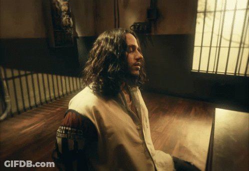 Man With Long Hair Sitting In Room Wearing U.S. Army Jacket GIF