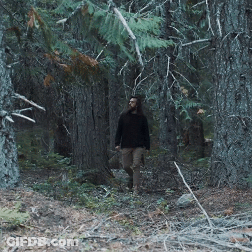 Man With Long Hair Walking Through Dark Forest GIF