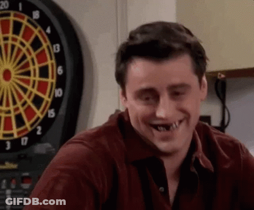Man With Missing Teeth Smiling In Front Of Dart Board GIF