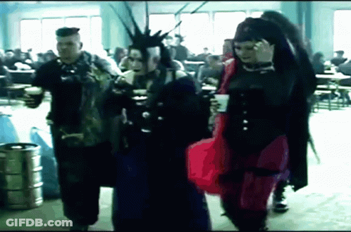 Man With Mohawk And Woman In Red Dress Walking In Crowded Room GIF