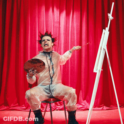 Man With Mohawk Sitting At Easel Holding Palette GIF
