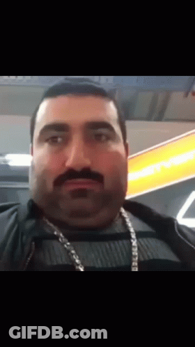 Man With Mustache And Chain Looking At Camera GIF