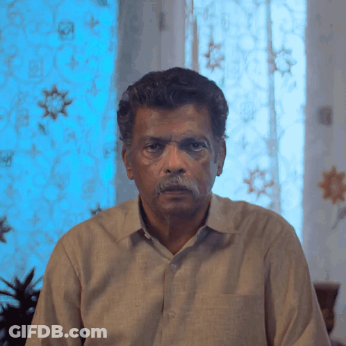 Man With Mustache Looking At Camera In Front Of Blue Curtain GIF