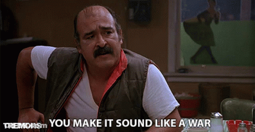 Man With Mustache Sitting At Table Saying You Make It Sound Like A War GIF