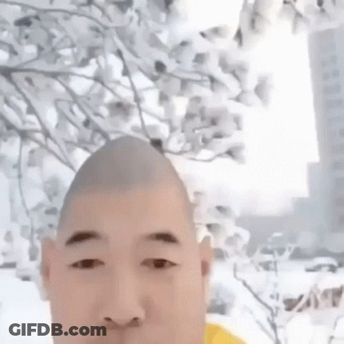 Man With Shaved Head Standing In Front Of Flowering Tree GIF