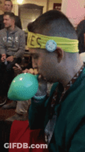Man With Yes Headband Blowing Up Green Balloon GIF