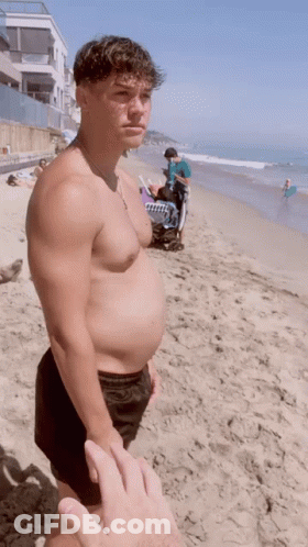 Man Without Shirt Holding Towel On Beach GIF