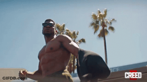 Man Without Shirt Standing In Front Of Creed Building GIF