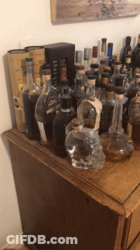Many Bottles Of Liquor Are On A Wooden Table Including A Bottle Of Whiskey Called Kentucky Straight GIF