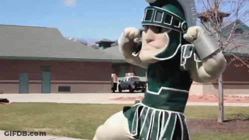 Mascot In Spartan Costume In Front Of Brick Building GIF