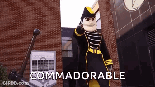 Mascot Standing In Front Of Brick Building Saying Commadorable GIF