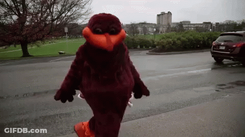 Mascot Walking Down Street In Front Of Parking Lot GIF