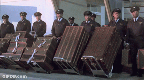 Men Carrying Luggage With Arrivals & Departures Sign GIF