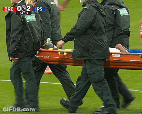 Men Carrying Stretcher On Soccer Field Scoreboard Says Bre 0 2 Ips GIF