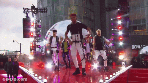 Men Dancing On Stage In Front Of Devil's Building GIF