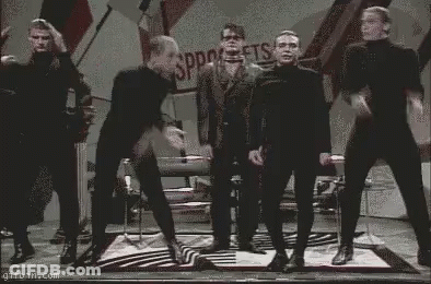 Men In Black Jumpsuits Dancing On Stage GIF