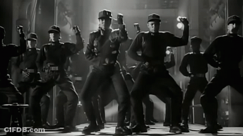 Men In Black Uniforms Dancing On Stage GIF