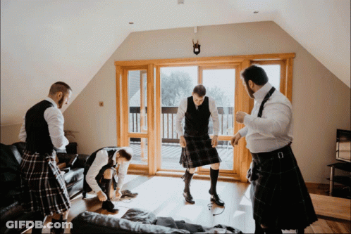 Men In Kilts Standing In Living Room GIF