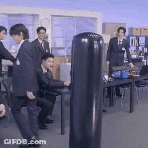 Men In Suits Standing Around Punching Bag GIF