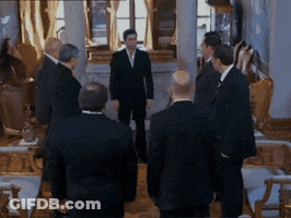 Men In Suits Standing Around Table GIF