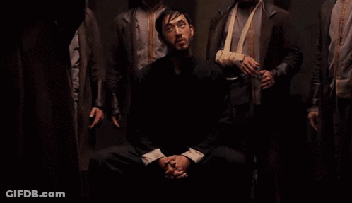 Men Standing Around Seated Man In Dark GIF