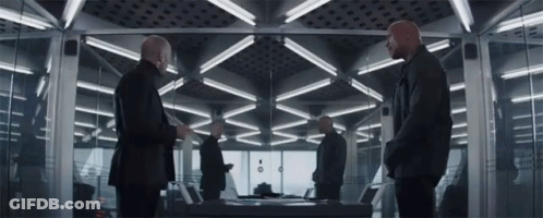 Men Standing In Room With Table And Mirror GIF