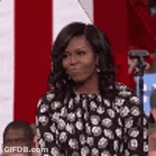 Michelle Obama In Black And White Polka Dot Dress In Front Of Red And White Flag GIF