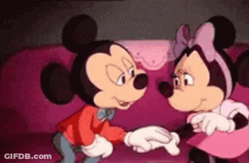 Mickey Mouse And Minnie Mouse Are Standing Next To Each Other On A Pink Couch Holding Hands . GIF