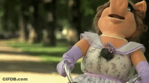 Miss Piggy From The Muppet Show Is Riding A Bike In The Park . GIF