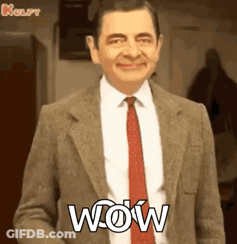 Mr Bean Is Wearing A Suit And Tie And Smiling With The Word Wow Written On His Chest . GIF