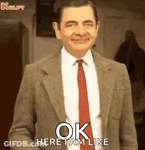 Mr Bean Smiling In Suit And Tie Saying Ok Here I Am GIF