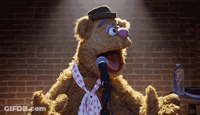 Muppet Fozzie Bear Singing Into A Microphone With A Brick Wall In The Background GIF