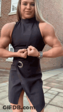 Muscular Woman In Black Dress In Front Of Brick Building GIF