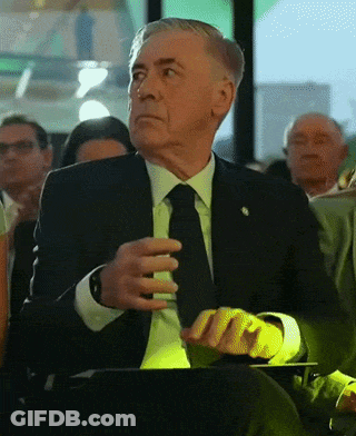 Older Man In Suit And Tie Sitting In Crowd GIF