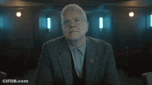 Older Man In Suit Arms Crossed Dark Room GIF