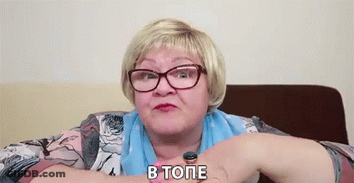 Older Woman In Glasses And Blue Scarf Sitting With Arms Crossed GIF