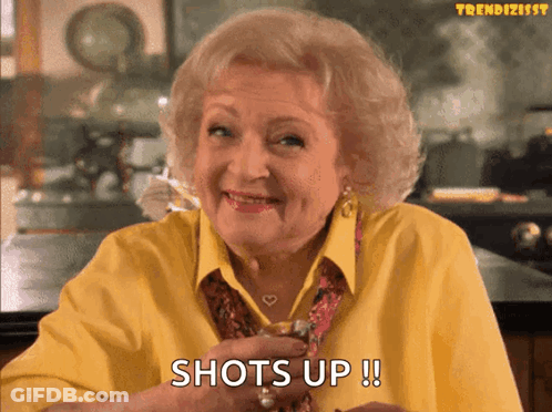 Older Woman In Yellow Holding Shot Glass Says Shots Up GIF