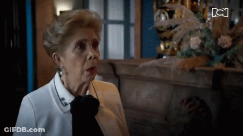 Older Woman Sitting By Fireplace With Clock GIF