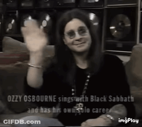Ozzy Osbourne Is Sitting On A Couch Waving His Hand . GIF