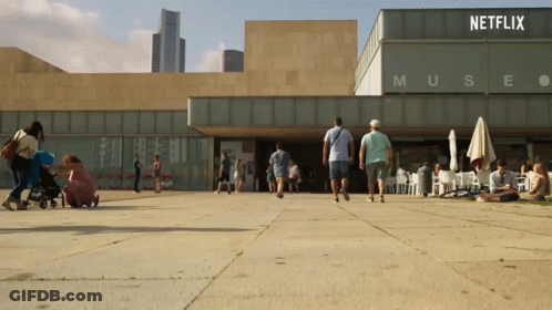 People Are Walking In Front Of A Building That Says Muse GIF