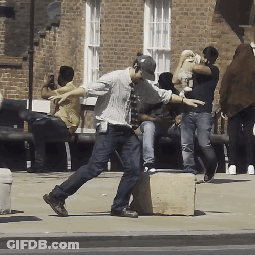 People Gathered On Sidewalk In Front Of Brick Building GIF
