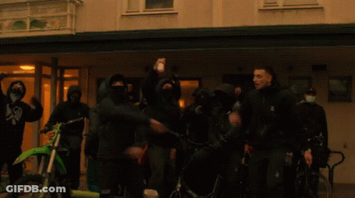 People In Front Of Building With Mask Saying A GIF