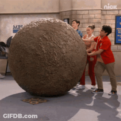 People Pushing Large Rock Near Niox Sign GIF