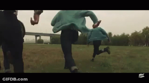 People Running Through Grassy Field In Front Of Bridge GIF