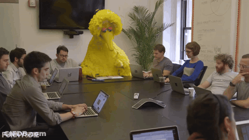 People Sitting At Table With Yellow Sesame Street Character GIF