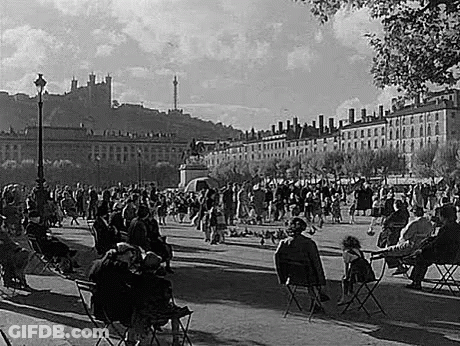 People Sitting At Tables In Park With Castle GIF