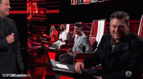People Sitting In Chairs On Stage With NBC Logo GIF