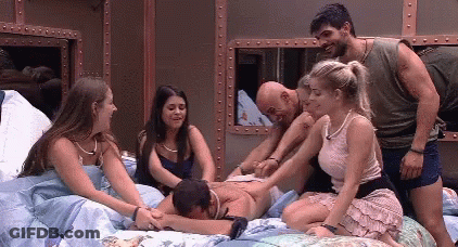 People Sitting On Bed With Man Lying On Back GIF